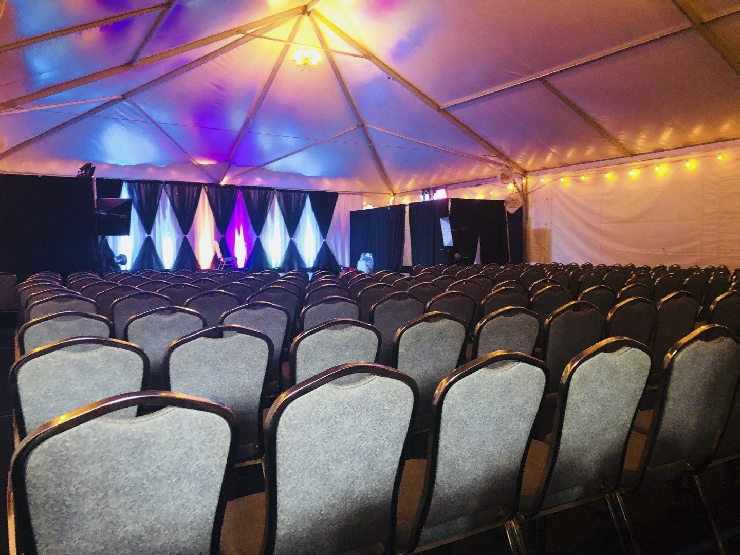 rows of chairs under a tent with lights