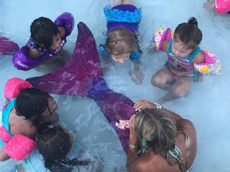 a group of children in the water playing with mermaid tails