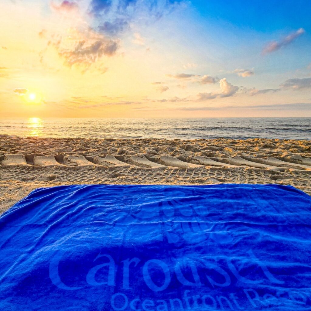 a blanket on a beach with the sun setting in the background